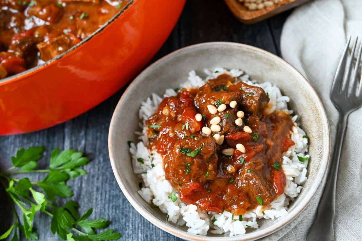 a bowl of marrakesh beef with pine nuts over rice with a fork and napkin