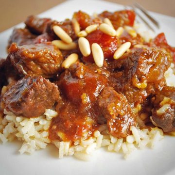 beef in sauce topped with pine nuts over rice on a white plate