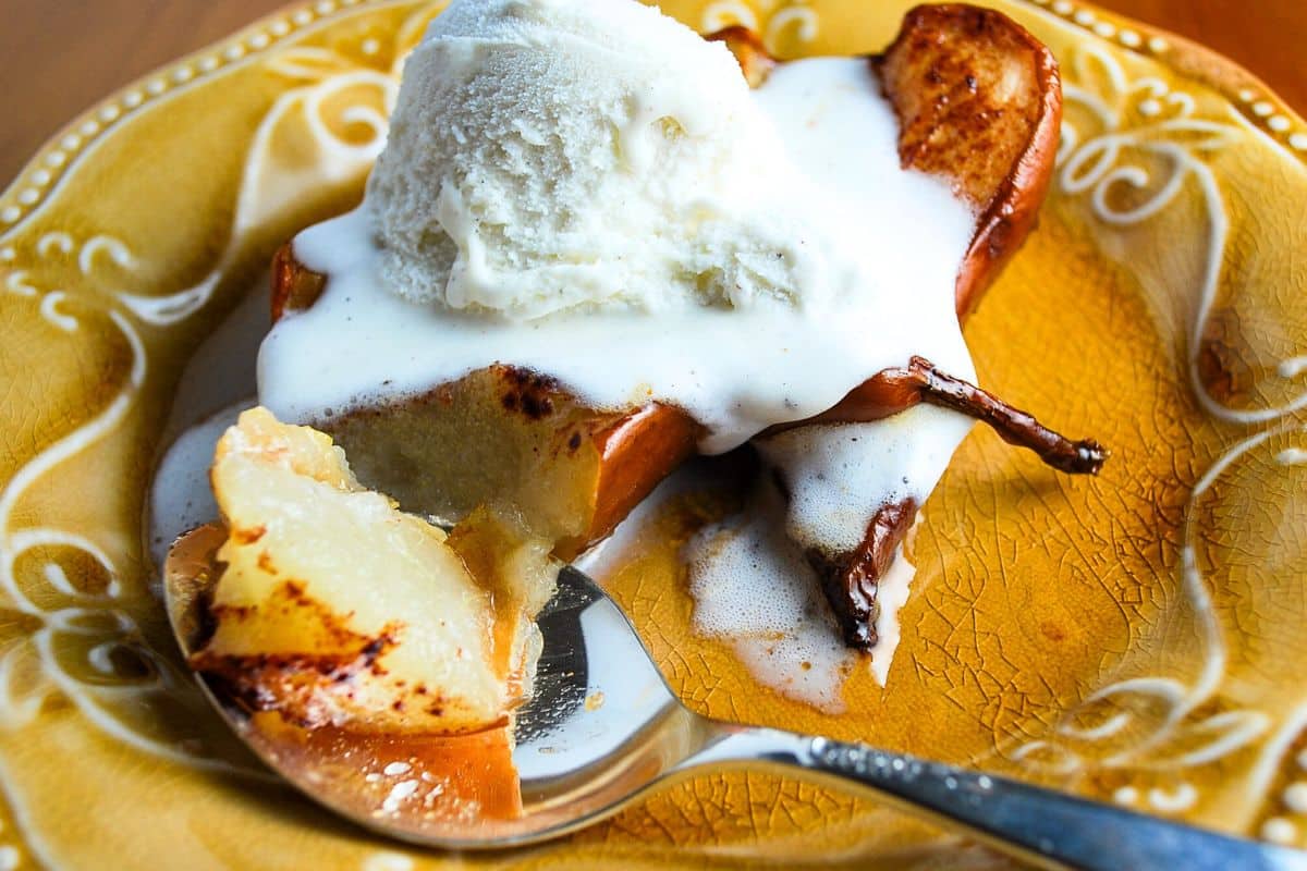 baked pears on a plate with a scoop of vanilla ice cream and a spoon with a bite cut off