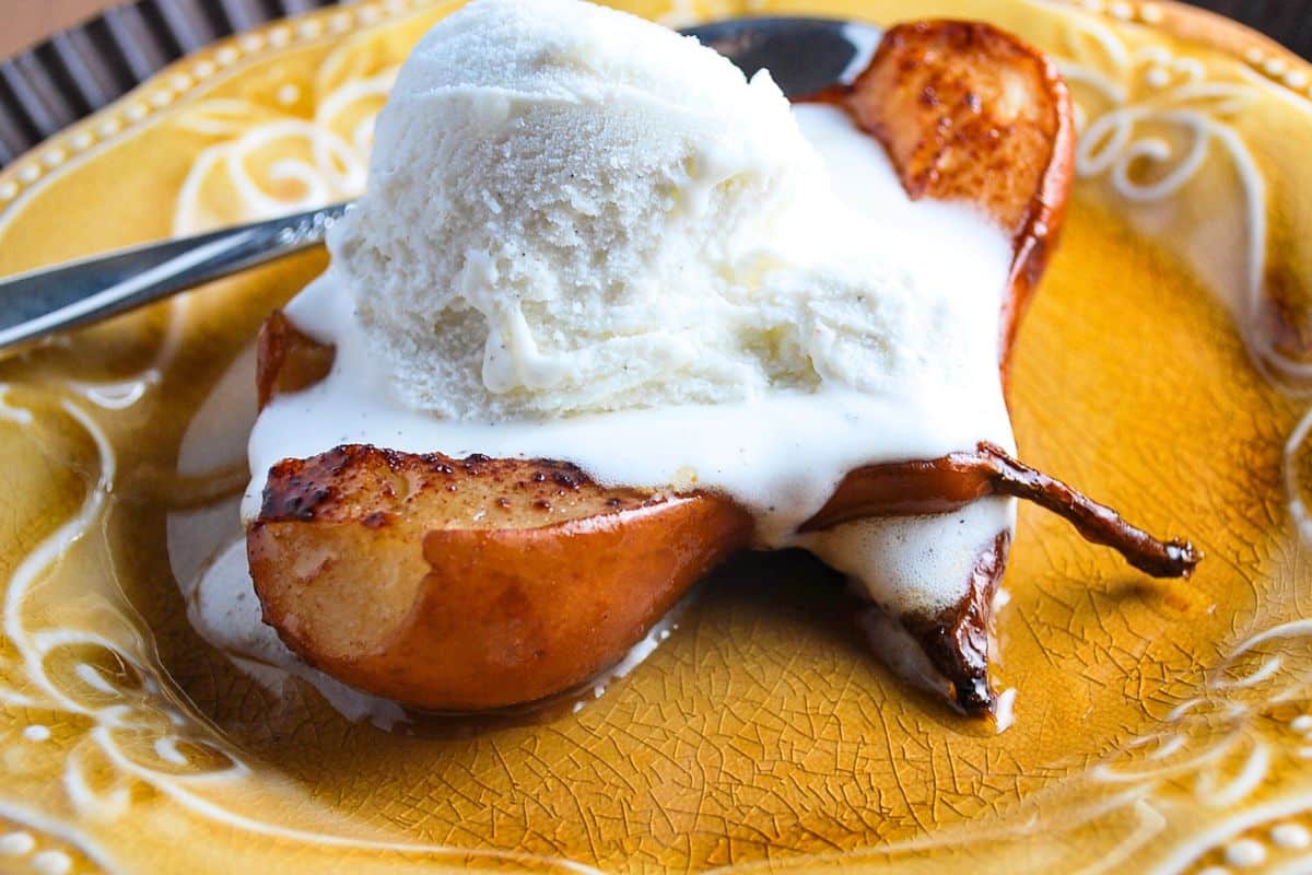 a scoop of ice cream on top of a sliced baked pear on a plate