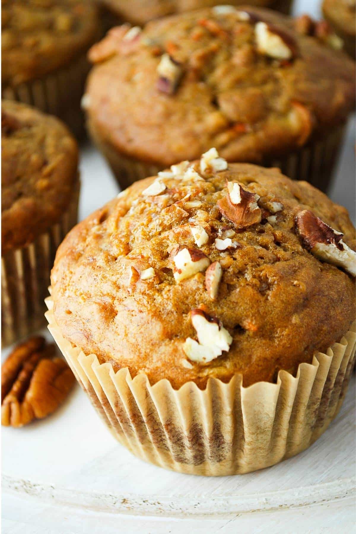 banana carrot muffins topped with chopped pecans on a white distressed platter