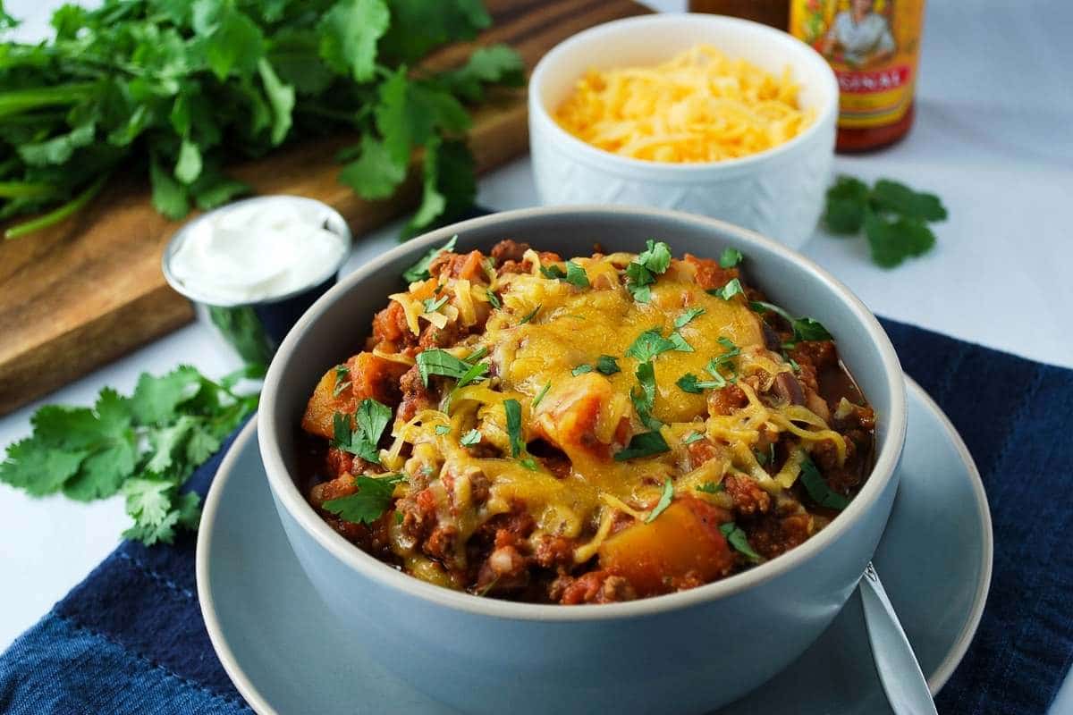chili in a gray bowl topped with cheese and cilantro with cheese in the background