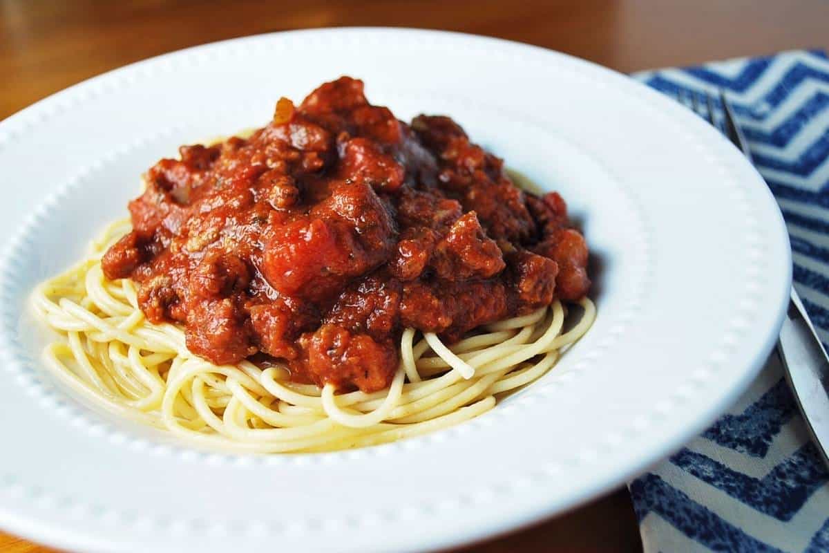 photo of spaghetti topped with sauce in a white bowl with a napkin and fork