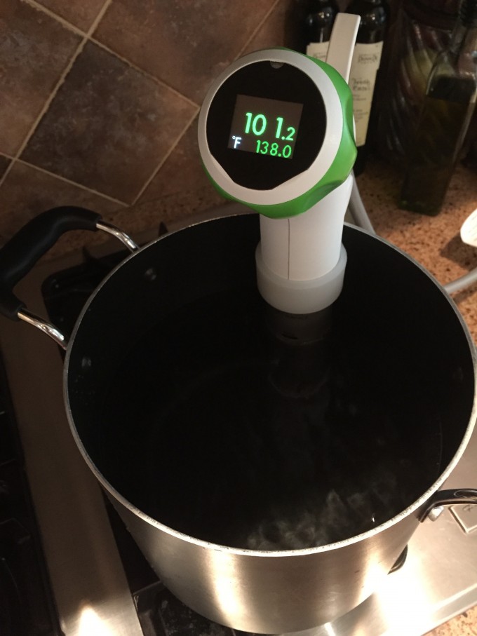 Nomiku sous vide cooker in a pot with water