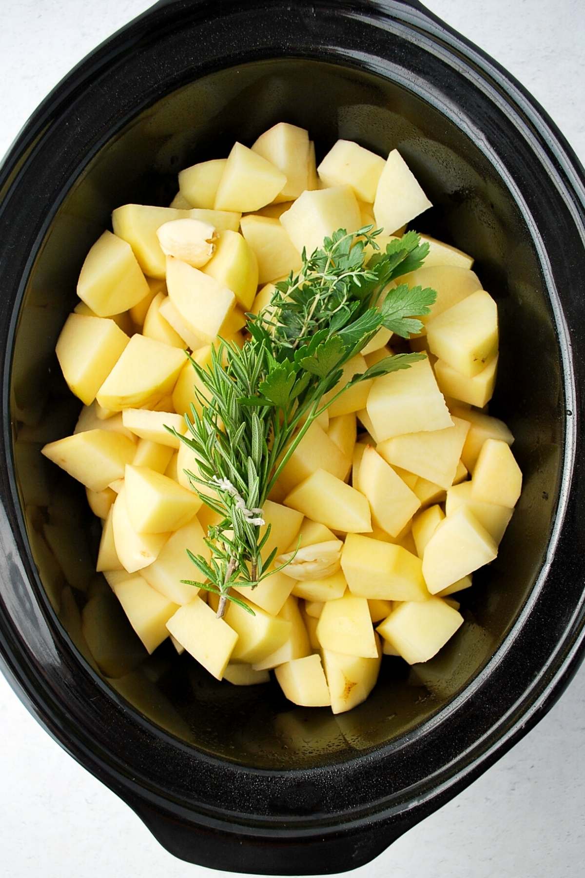 chopped potatoes and a bundle of herbs in a slow cooker insert
