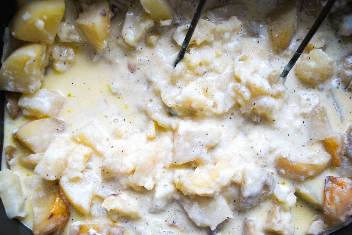 mashed potatoes with butter, milk and cheese in a slow cooker with a potato masher