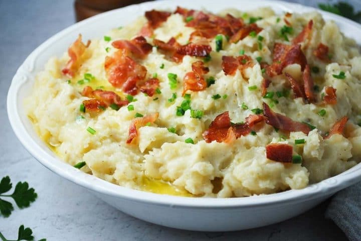 side view of loaded mashed potatoes with bacon and chives in a white bowl