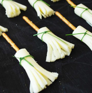 string cheese cut in the shape of a broom with a pretzel stick on top and a chive wrapped around it