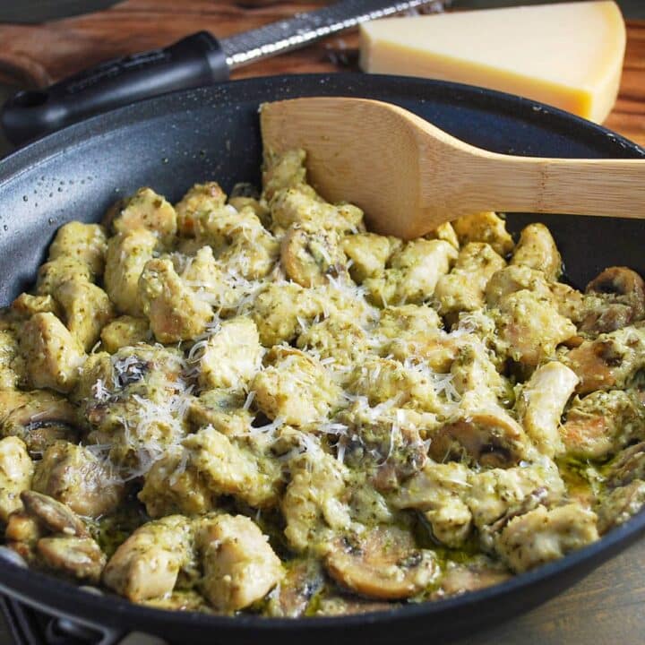 close up photo of pesto chicken with mushrooms in a skillet with a block of fresh parm behind it