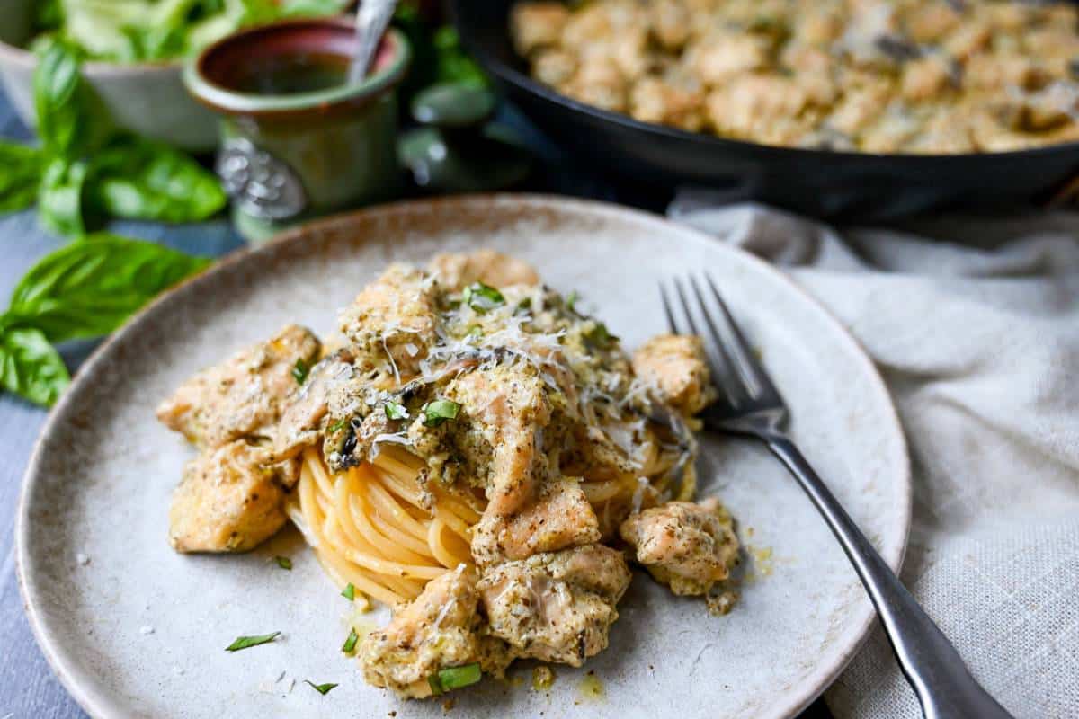 chicken in pesto sauce on spagetti with a skillet of pesto chicken in the background