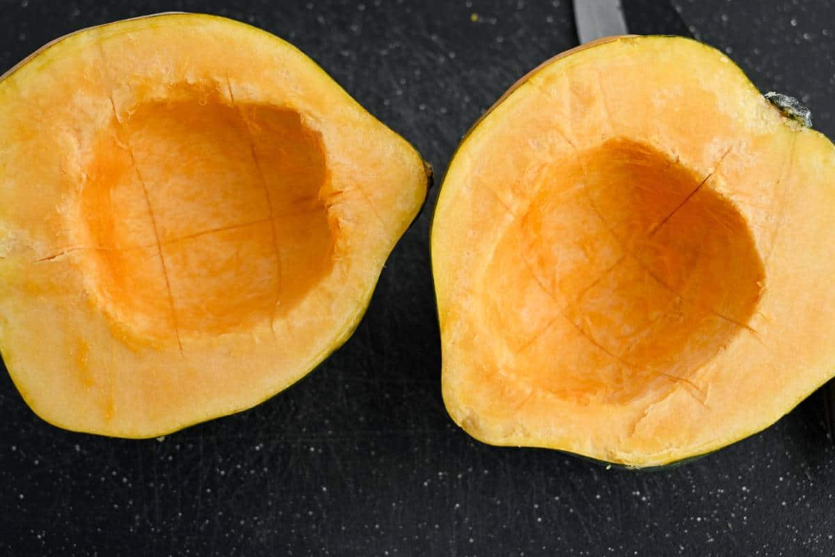 an acorn squash sliced in half, seeded and scored for cooking