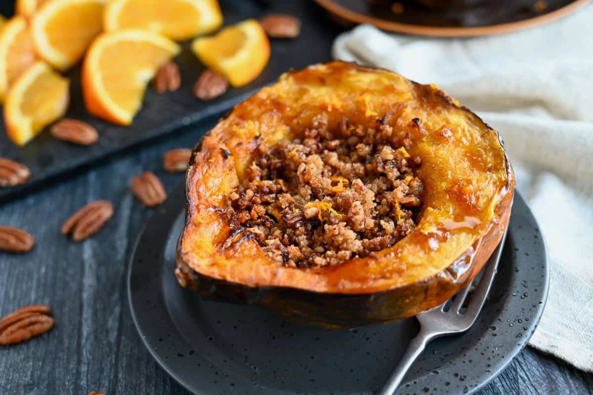 a stuffed air fried acorn squash drizzled in maple syrup and sprinkled with fresh orange zest on a black plate with a fork