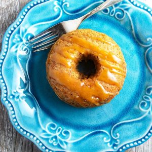 a baked maple donut on a blue plate drizzled with maple glaze