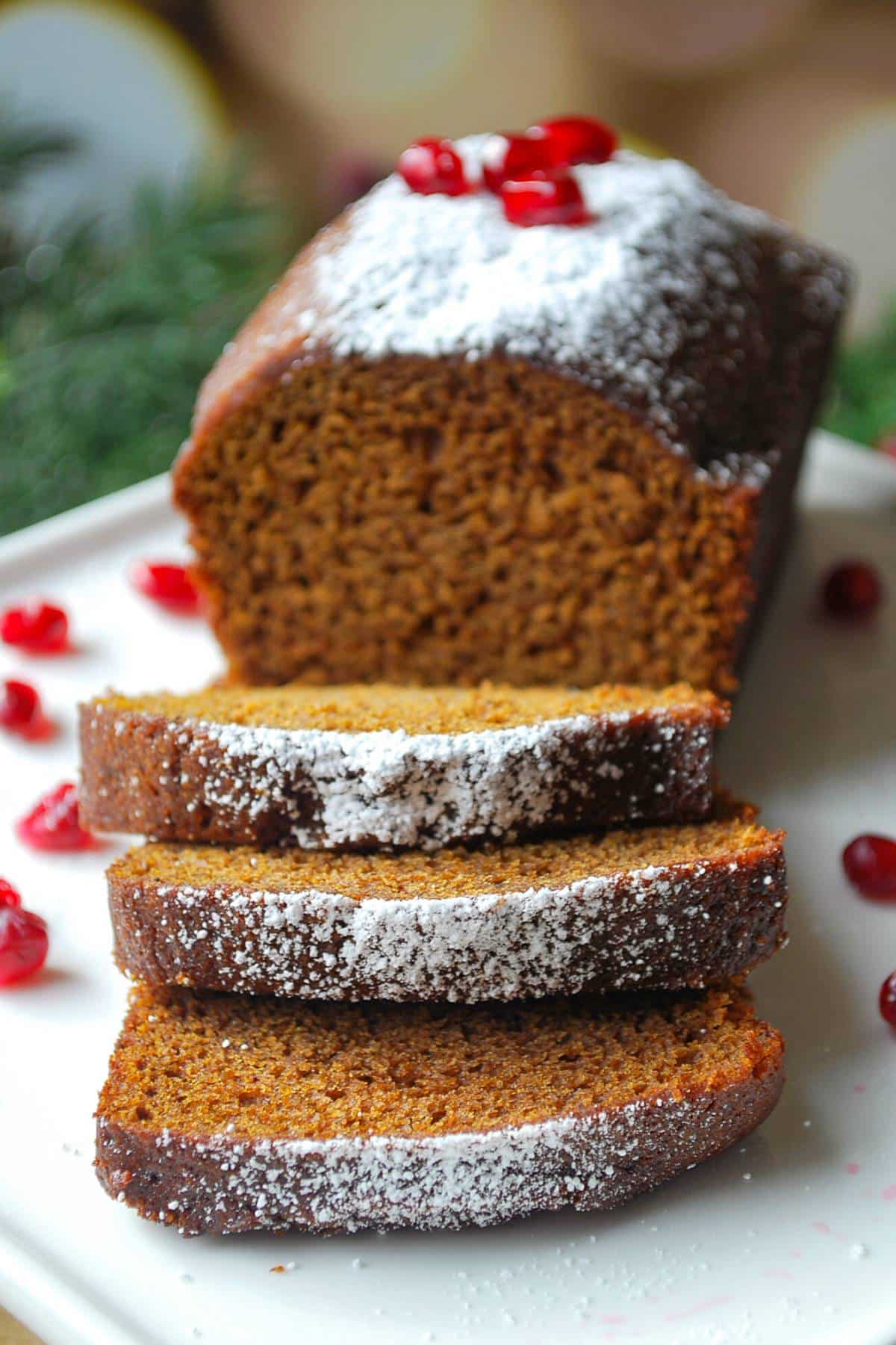 close up of a sliced gingerbread loaf with greenery in the background