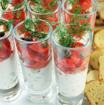 close up of mini glasses with a Greek yogurt mixture on the bottom with smoked salmon, capers, and sprigs of dill on top