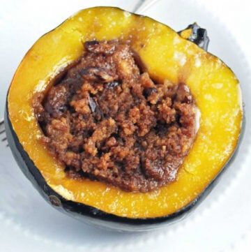 close up of half of a cooked acorn squash with stuffing in a white bowl