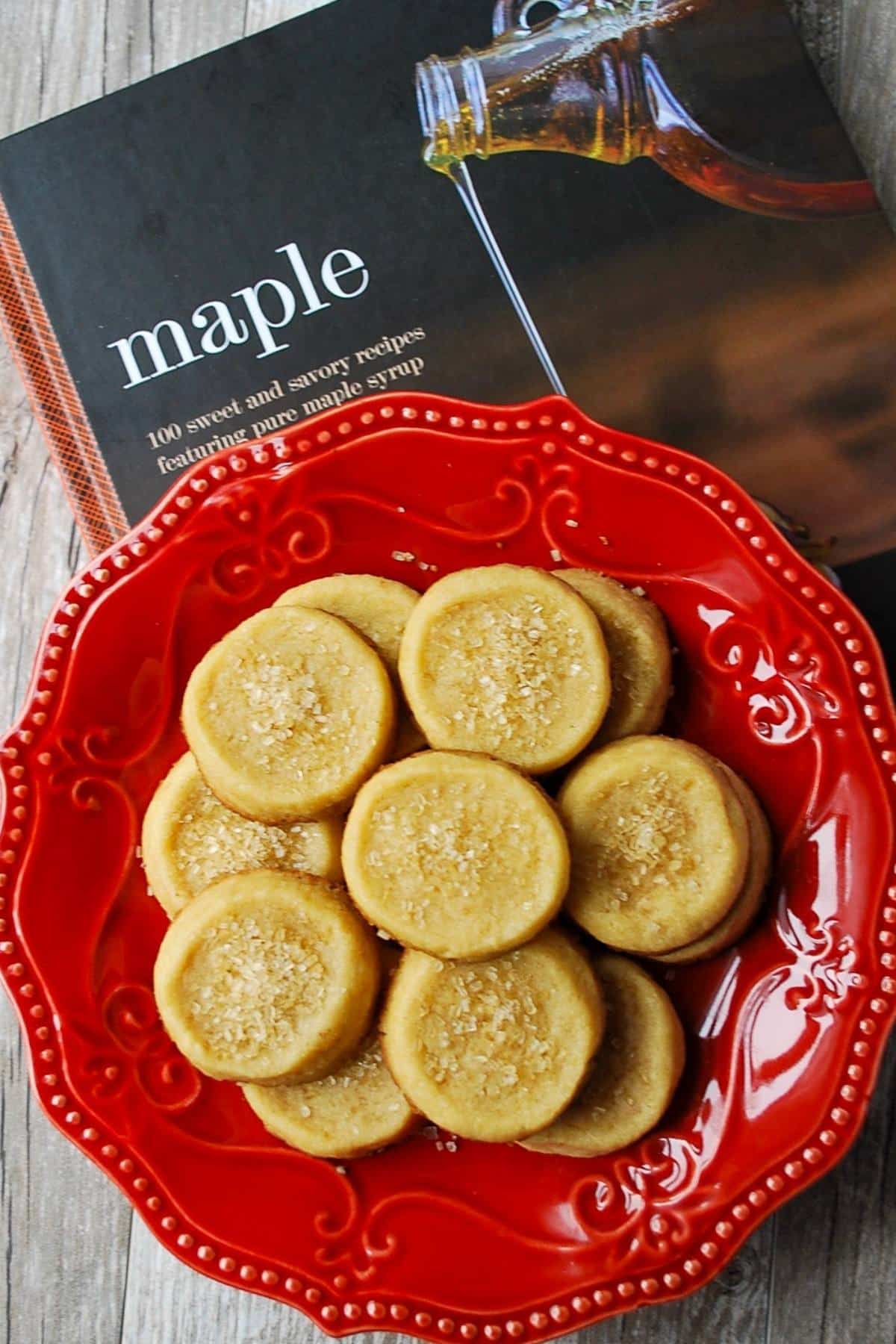 close up of a red plate of maple shortbread cookies with a maple cookbook underneath it