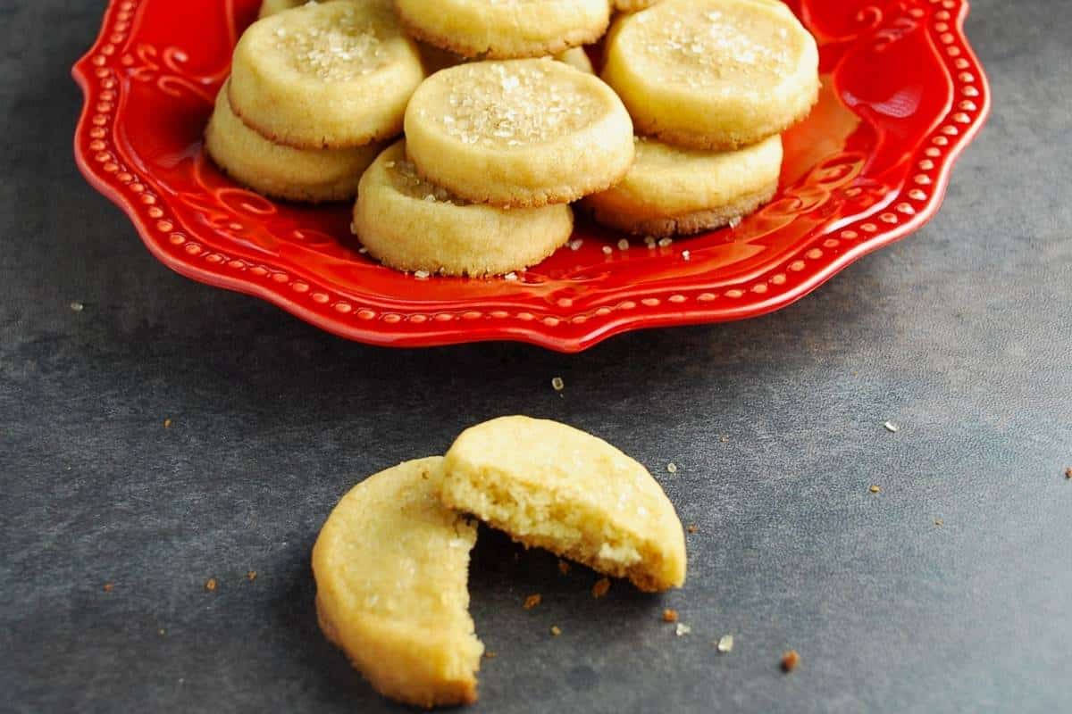 a maple shortbread cookie broken in half in front of a plate of cookies