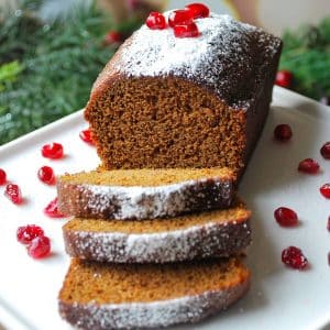 a sliced loaf of gingerbread dusted with powdered sugar and garnished with pomegranate seeds