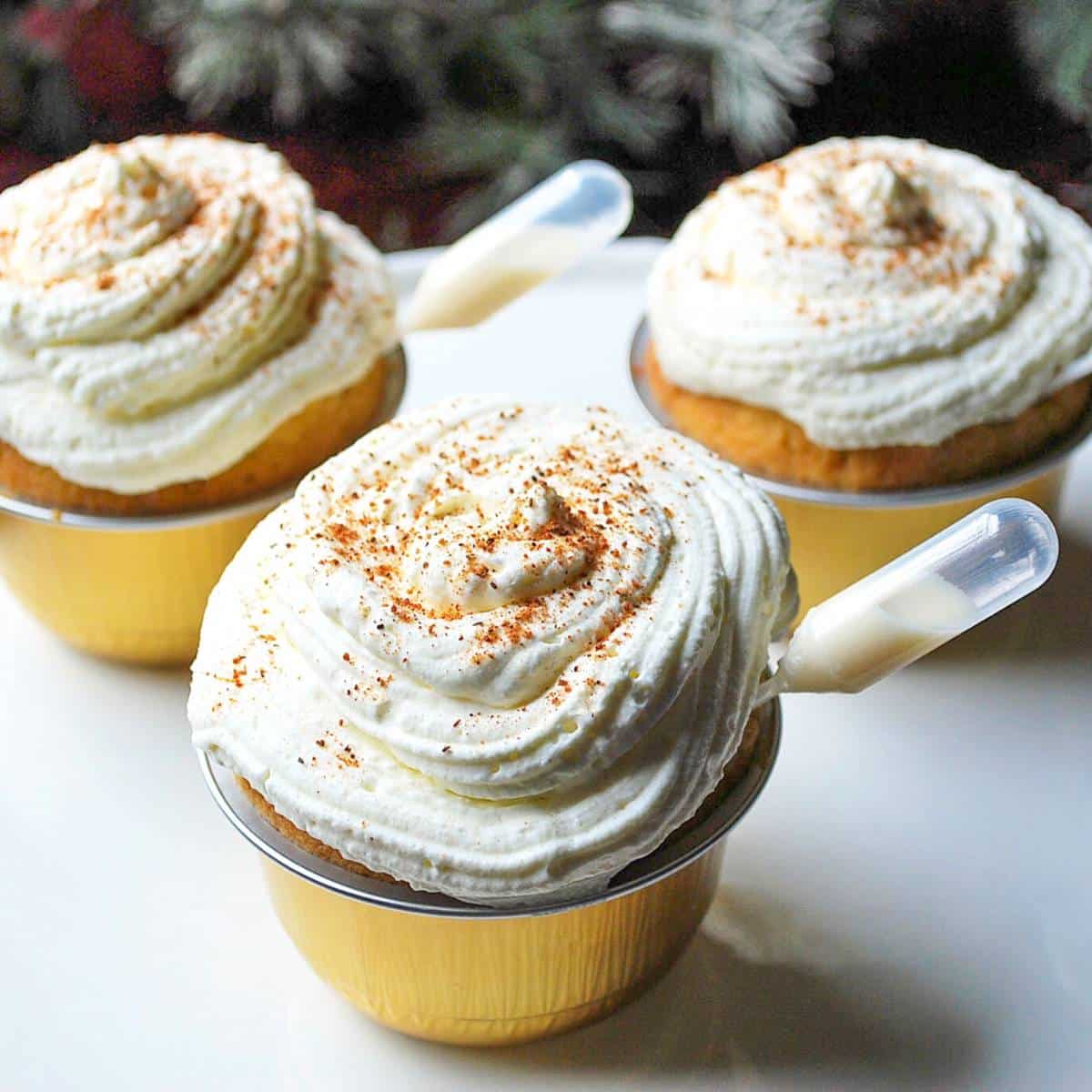 close up of three eggnog cupcakes on a platter with pipettes full of rum cream
