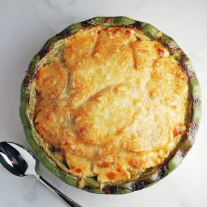 potato gratin baked in a pie plate with a spoon for serving