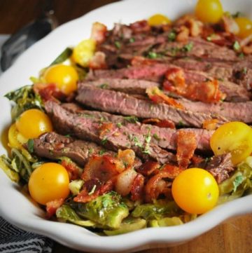 close up of steak salad in a white serving bowl garnished with yellow cherry tomatoes and chopped bacon