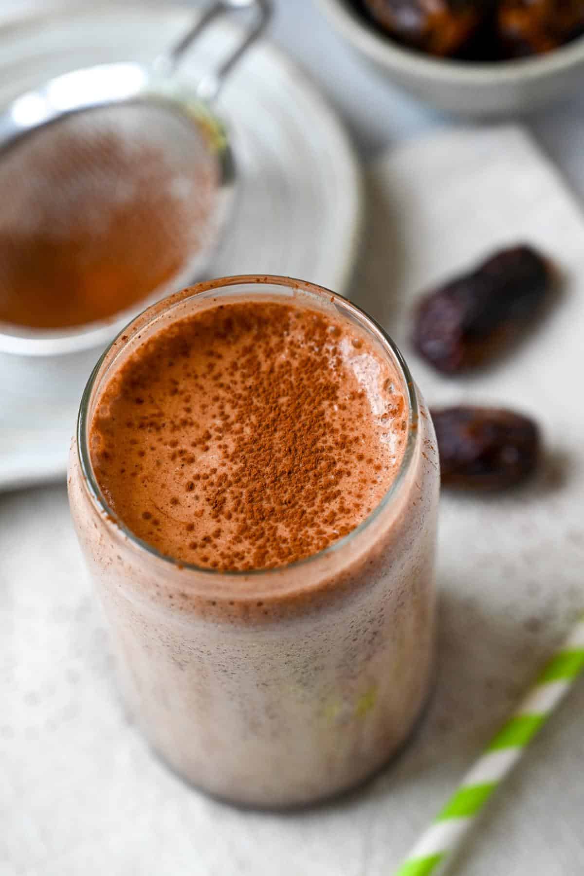 overhead photo of a chocolate date protein shake with a green striped straw and a dusting of cocoa powder