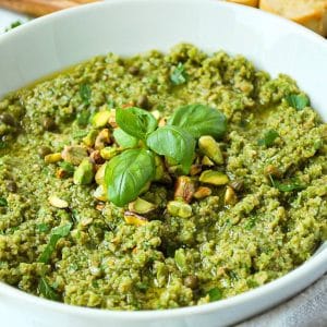 green olive tapenade topped with pistachios and fresh basil in a white bowl