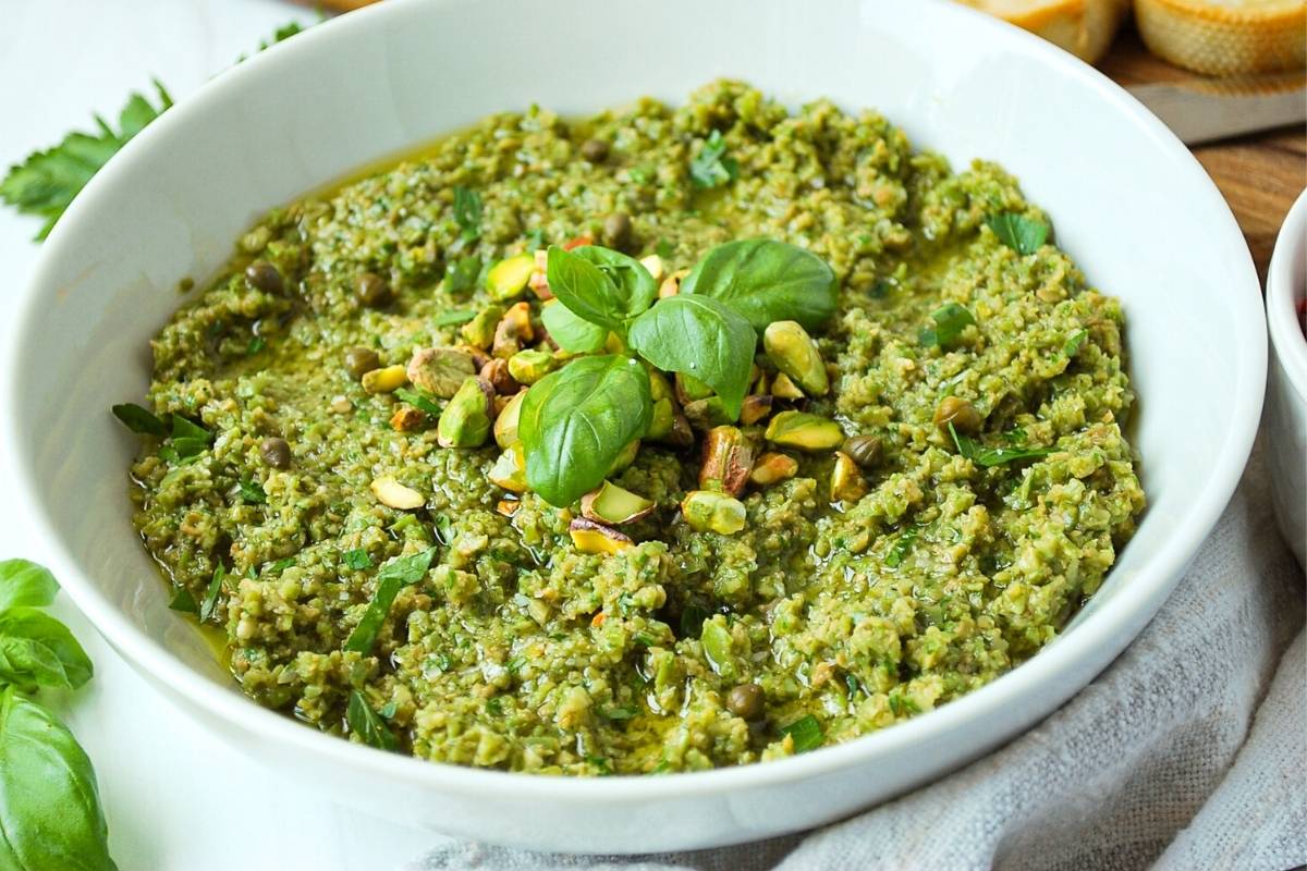 green olive tapenade in a white serving bowl with fresh basil around it
