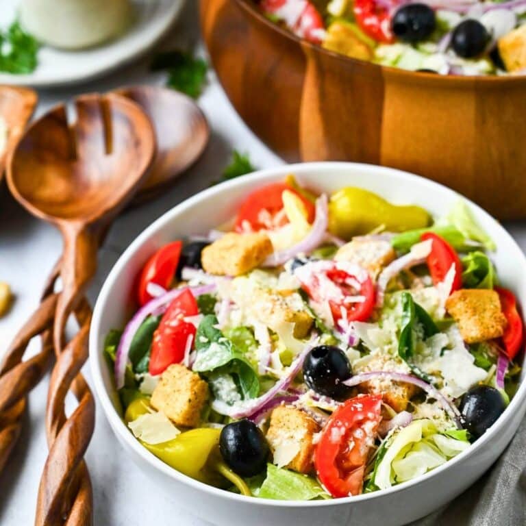olive garden salad in a bowl with tongs and a jar of dressing with a large serving bowl of salad