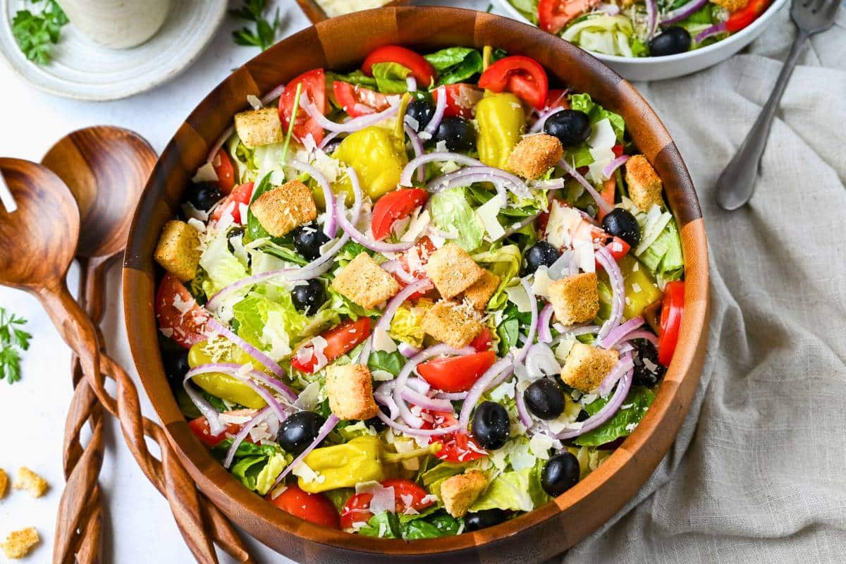 a large wooden salad bowl with an olive garden salad and tongs 