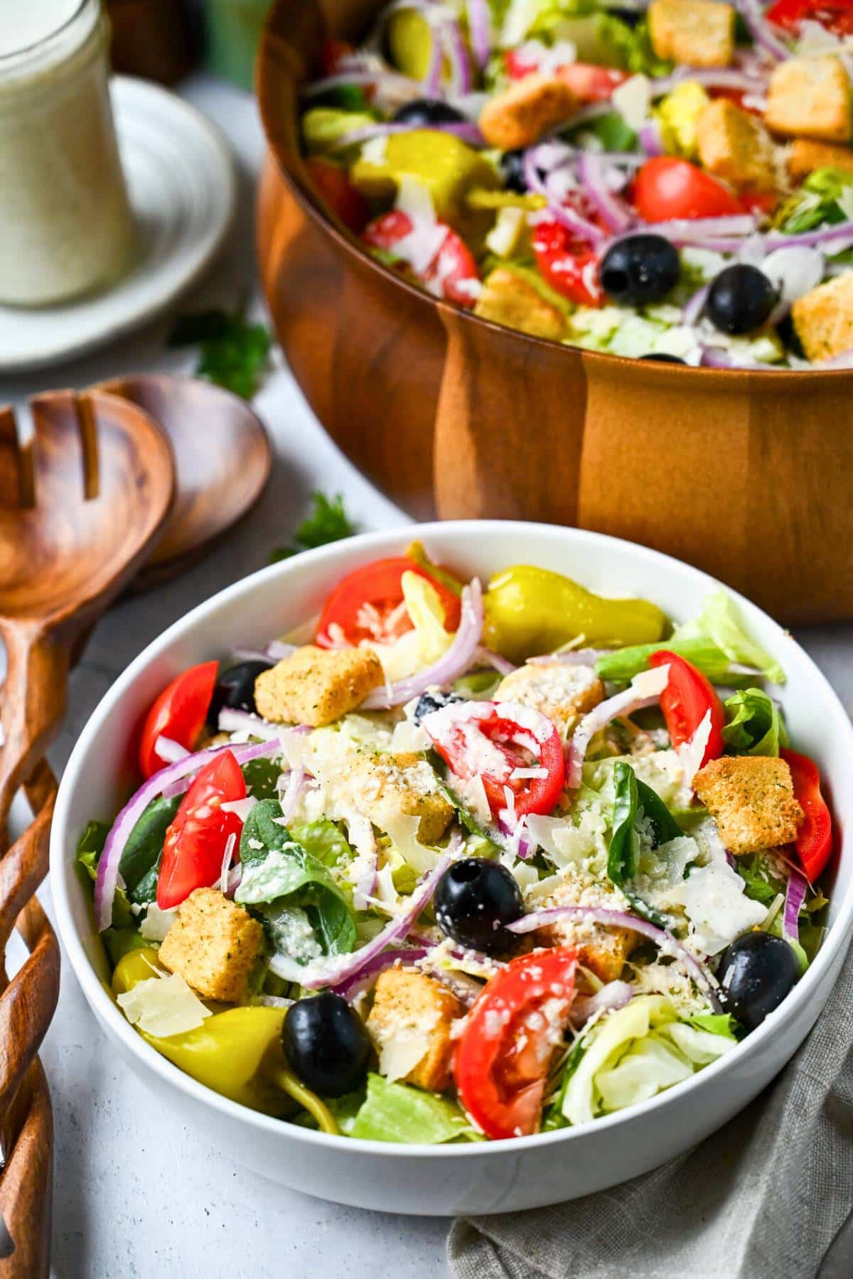 a served bowl of salad with a bowl of salad, and jar of dressing behind it
