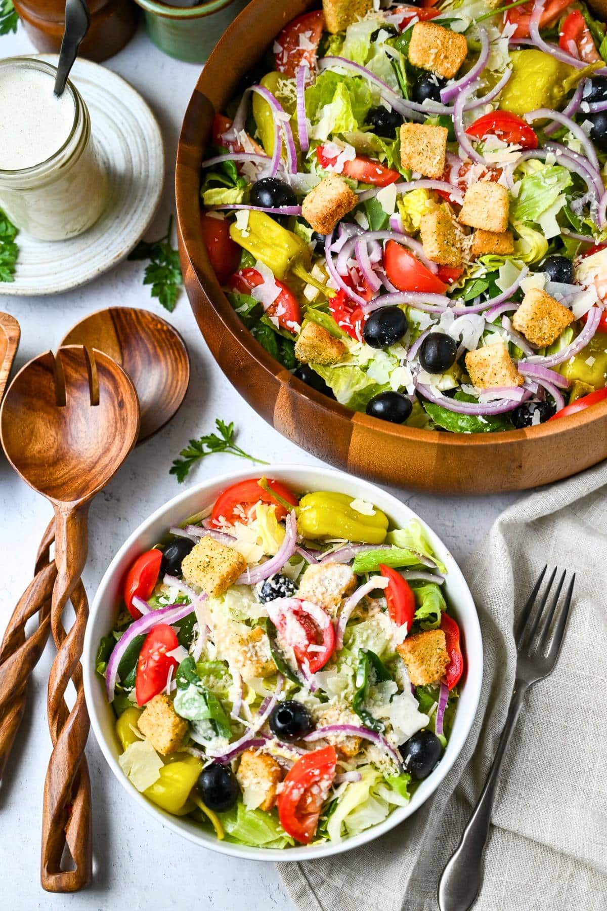 looking down at a bowl of salad with a serving bowl of salad and a jar of dressing