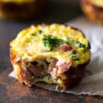 an egg muffin with ham and kale with a bite out of it on top of a napkin
