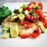 grilled halibut filet topped with avocado relish with a sprig of fresh parsley on the side