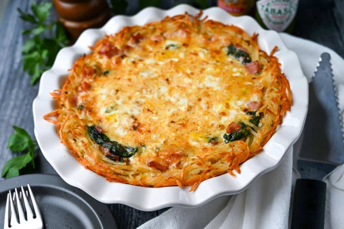 a freshly baked quiche with golden hash brown crust with plates and forks