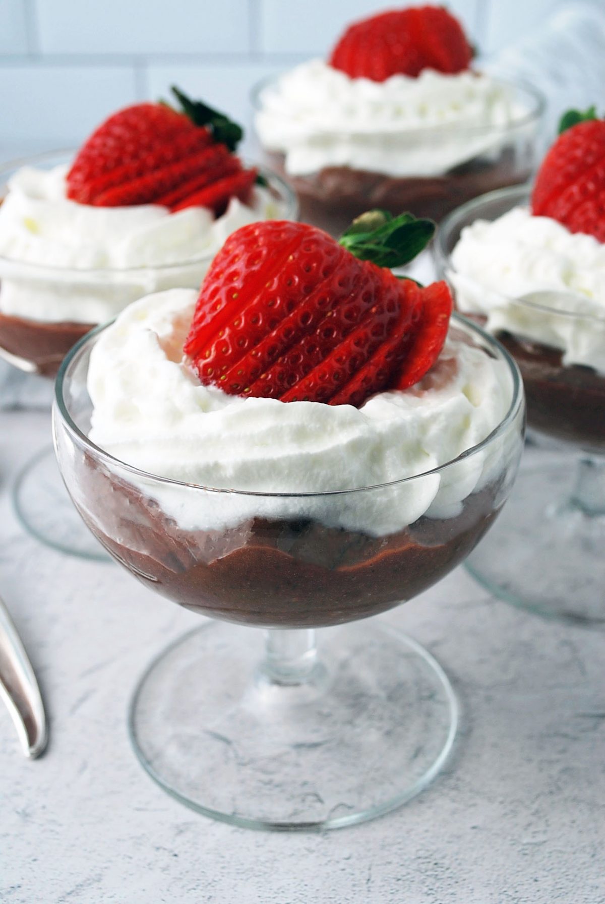 Four parfait glasses with chocolate pudding, whipped cream and a strawberry on top