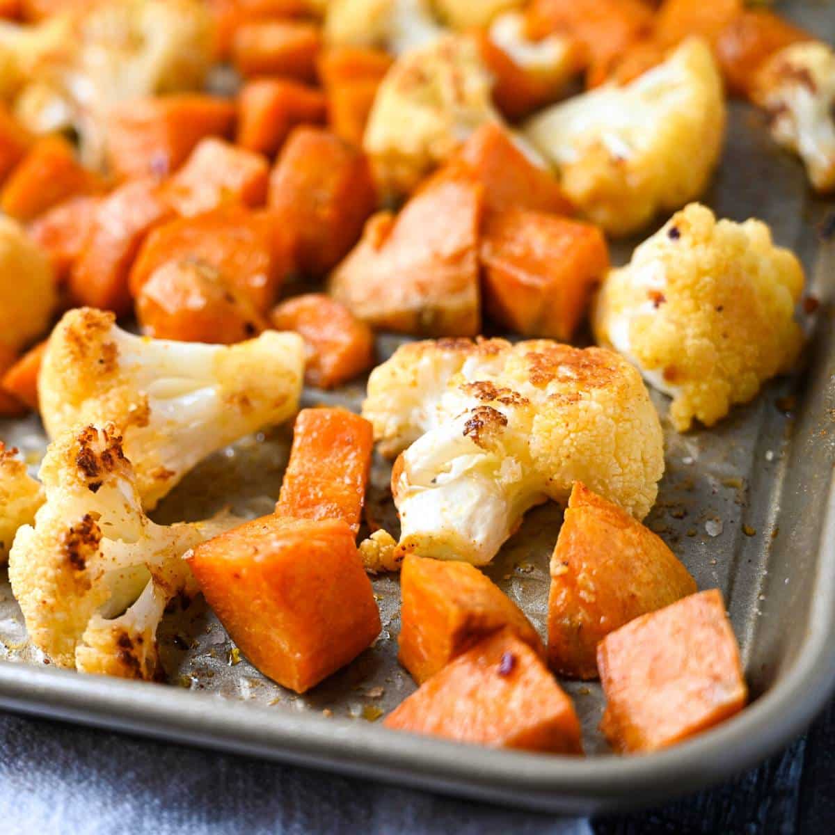 close up of the side of a roasting pan with sweet potatoes and cauliflower perfectly roasted