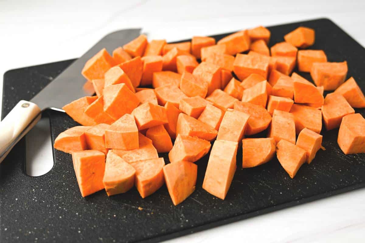 chopped sweet potatoes on a black cutting board with a knife