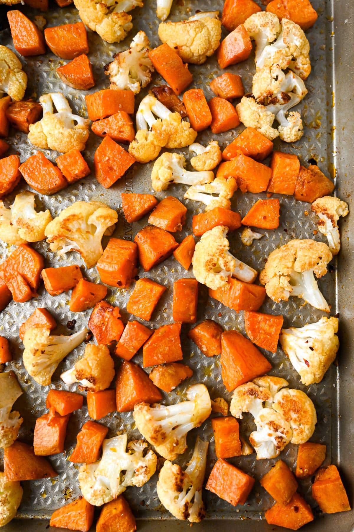 a roasting pan with caramelized sweet potato cubes and cauliflower florets