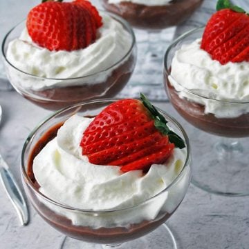 chocolate pudding topped with whipped cream and a sliced strawberry in parfait glasses