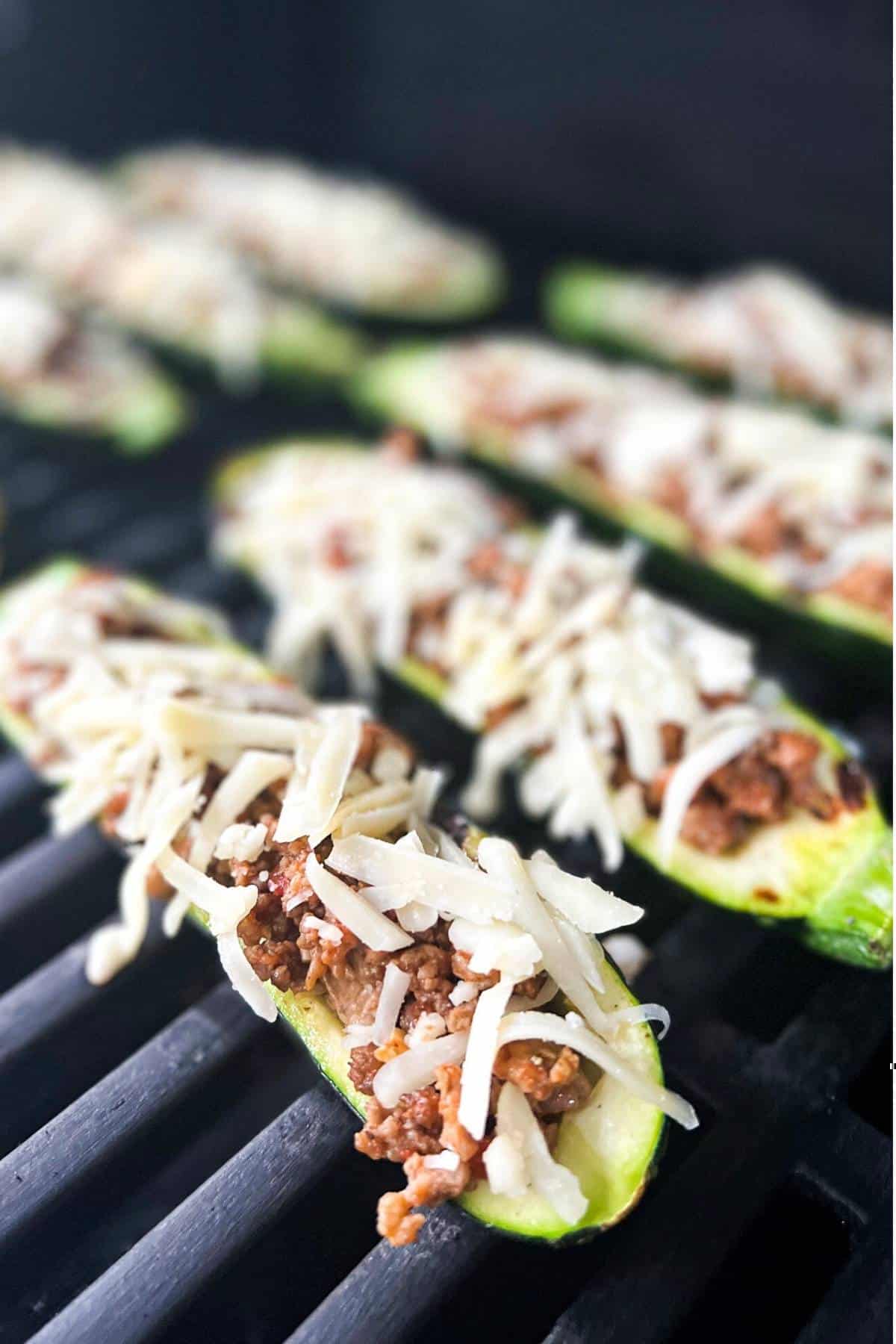 stuffed zucchini boats topped with cheese cooking on a grill