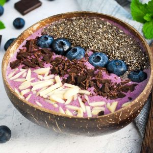 close up of a blueberry smoothie bowl topped with almonds, chocolate, blueberries, and chia seeds