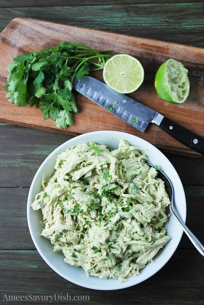 Avocado Chicken Salad in a bowl with sliced limes and cilantro on a cutting board