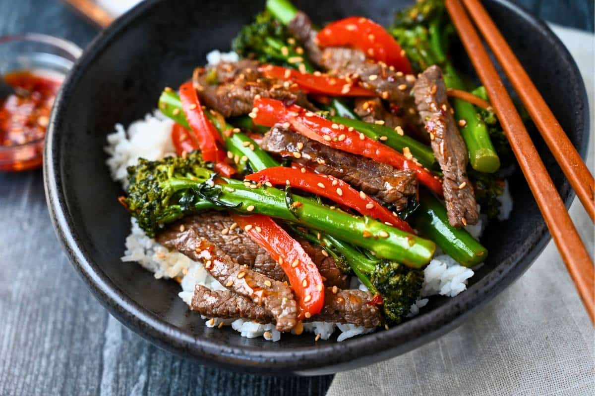 side view of a bowl of stir fry with a dish of chili garlic oil and a napkin