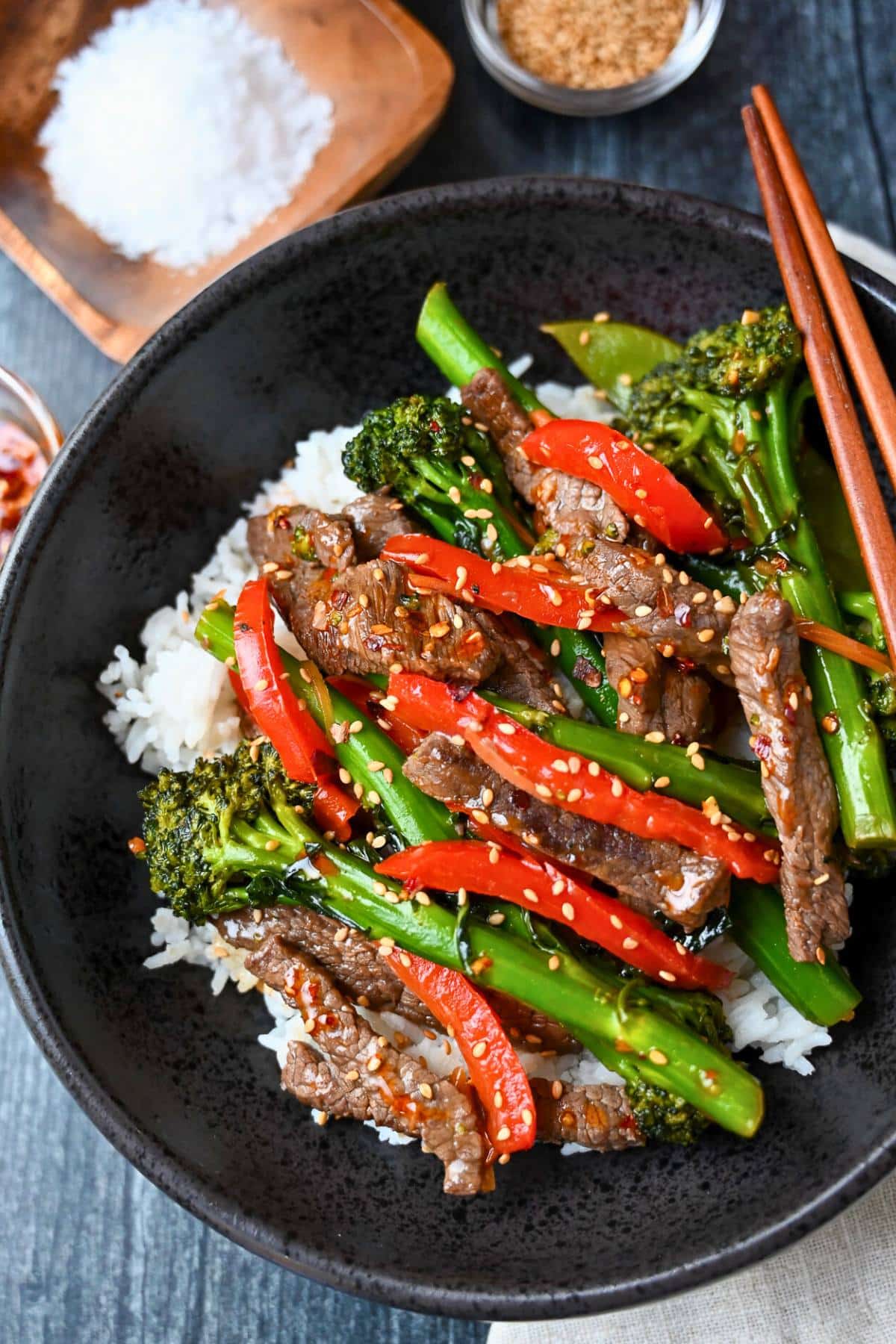 close up of a bowl of steak stir fry with broccolini and vegetables with chop sticks