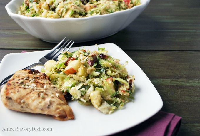 Brussels sprouts salad and chicken on a white plate with a fork and bowl in the background