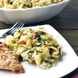 Brussels sprouts salad on a white plate with a grilled chicken breast and a fork