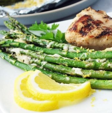 grilled asparagus on a white plate with grilled chicken and lemon