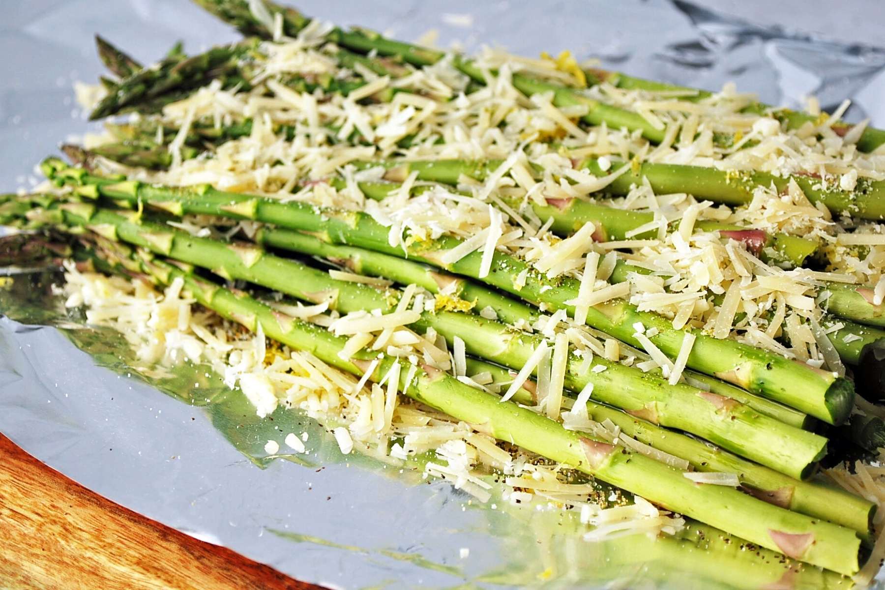 fresh asparagus on foil sprinkled with cheese, olive oil, and lemon zest